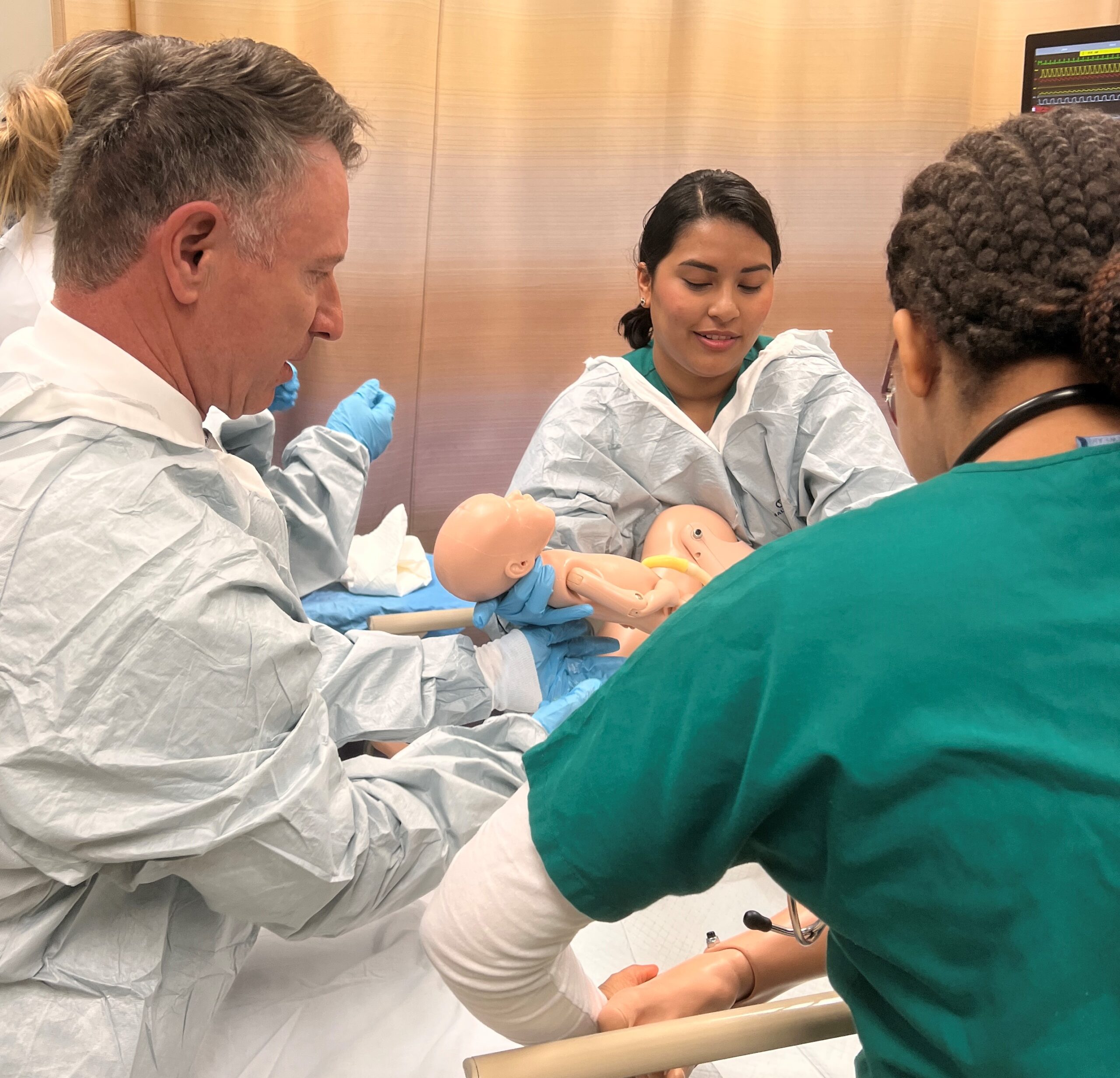 Dr. David Doré (left) and students participate in a simulated birth at one stop of the chancellor's visit to the college.